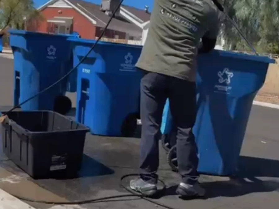 Perez Power Wash technician pressure washing a row of residential trash bins on the curb