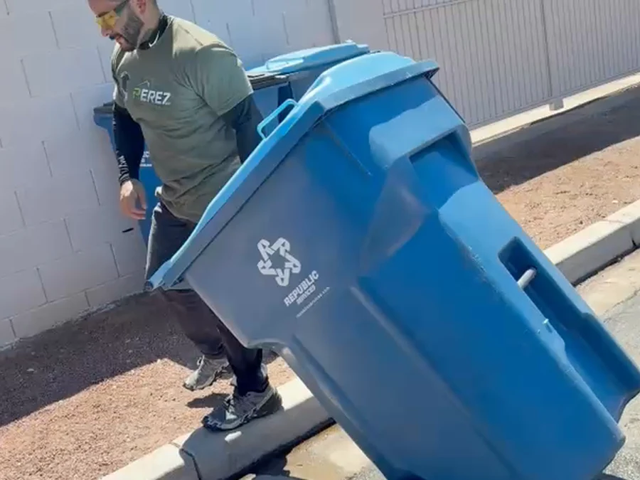 Perez Power Wash technician carrying a freshly cleaned trash bin back to the curb